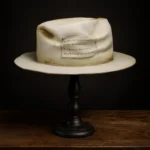 Left side view of beige Memento custom fedora hat showing stitched quote patch and distressed details