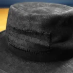 Close-up of black Memento fedora hat showing stitched patch with engraved quote
