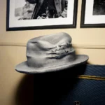 Gray Memento fedora hat showing engraved quote patch, displayed indoors beside framed photos
