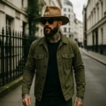 Male model wearing the Rooster Cogburn Replica Hat, a brown distressed felt fedora inspired by Jeff Bridges’ hat in True Grit (2010), styled with a green jacket and sunglasses.