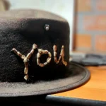 Close-up of the ScrewU handmade felt hat showing stitched “YOU” lettering and metal screw detail