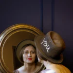 Woman wearing the ScrewU handmade felt hat looking into a mirror, showing stitched “YOU” detail