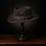 Side view of the handcrafted brown felt hat inspired by Margaret Dutton from the series 1883, displayed on a wooden stand.