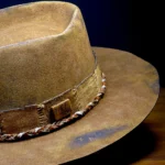 Close-up of brown western nomad hat showing braided cord and weathered felt texture