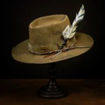 Brown western nomad hat with feather, cords, and playing card accent on wooden stand