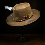 Right side view of brown western nomad hat with feather and braided cord band on wooden stand
